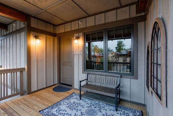 A wooden porch with a bench, a door, and a window with a view of houses.