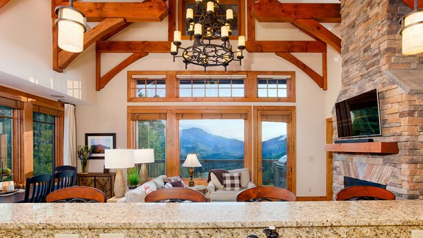 A spacious living area with a stone fireplace, wooden beams, and a large window overlooking mountains. - Breathtaking View - Fabulous & Well-Stocked Kitchen - Now renting for October🍁🍂🍁 (Boone)