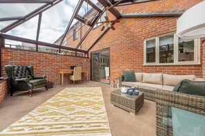 A spacious patio with a brick wall, a green leather chair, a wicker sofa, and a patterned rug.