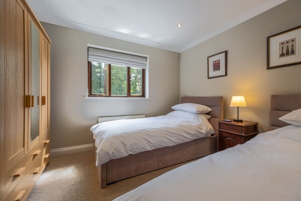 A bedroom with two beds, a wardrobe, a window with blinds, and a nightstand with a lamp. - The Innings, Burnham Deepdale, Norfolk (Burnham Deepdale)