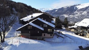 Ein Chalet mit geneigtem Dach, umgeben von schneebedeckten Bergen.