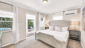 A bedroom with a bed, bedside tables, and an air conditioning unit. - Steps from Beach / Quaint Cottage / Hot Tub / Surf Key / H0MES (Fort Lauderdale)