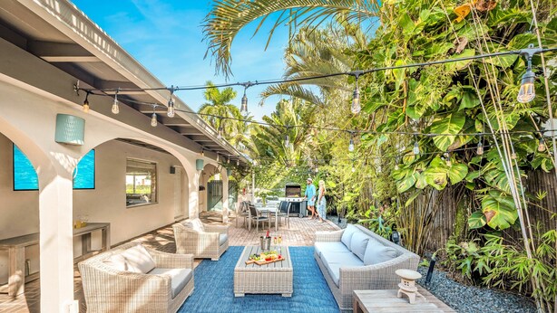 A covered outdoor patio with wicker furniture, a blue rug, and a barbecue area. - Steps from Beach / Quaint Cottage / Hot Tub / Surf Key / H0MES (Fort Lauderdale)