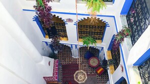 Une cour avec un sol carrelé, des plantes en pot et un espace de détente central agrémenté d’un tapis à motifs.