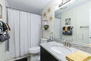 A bathroom with a white toilet, a shower curtain, a sink with a mirror, and towels on the wall.