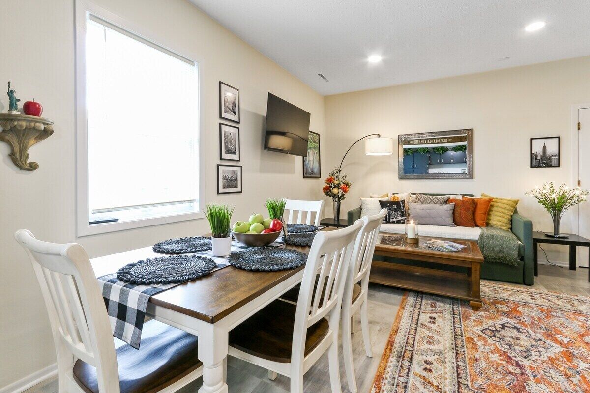 A dining area with a wooden table, white chairs, and a black and white checkered tablecloth. There is a bowl of fruit on the table and a decorative wall-mounted shelf with a statue.