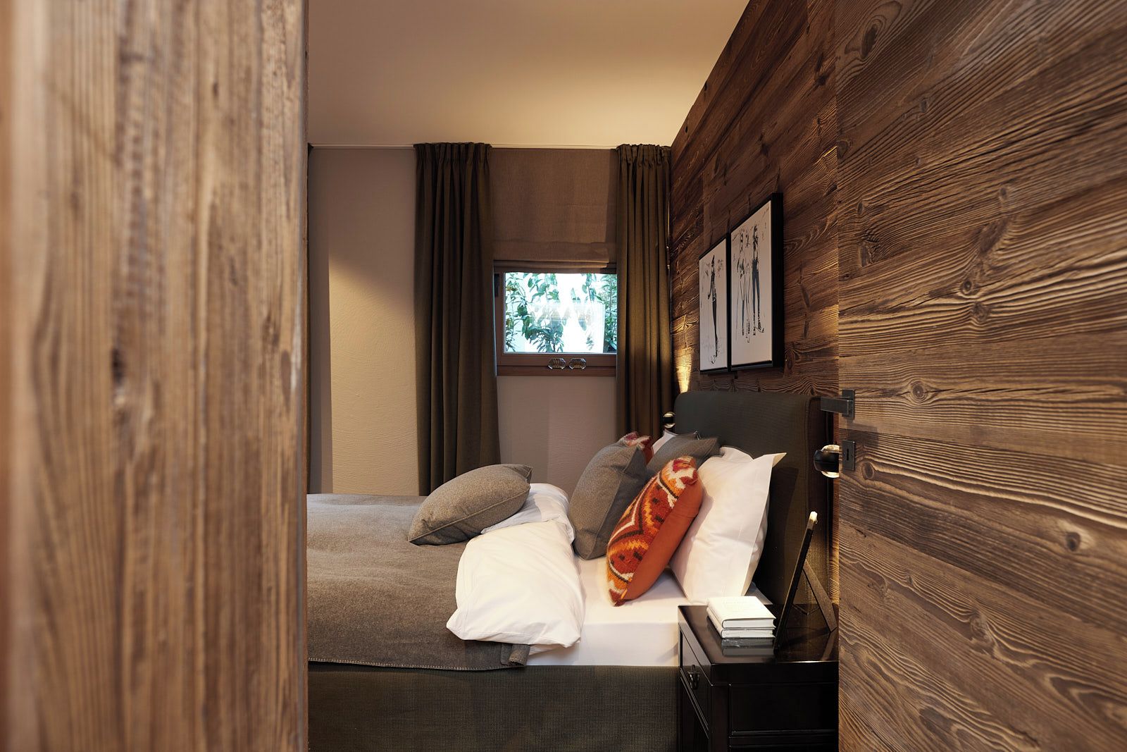 Ein modernes Schlafzimmer mit Holzwand, einem Bett mit vielen Kissen, einem Nachttisch und einem Fenster mit Vorhängen.
