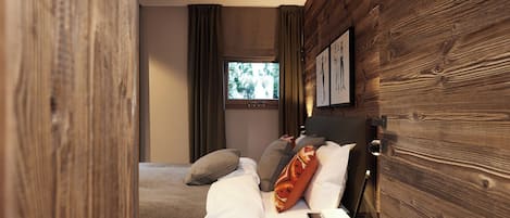Un dormitorio moderno con una pared de madera, una cama con varias almohadas, una mesita de noche y una ventana con cortinas.