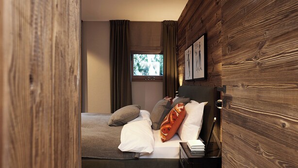 Ein modernes Schlafzimmer mit Holzwand, einem Bett mit vielen Kissen, einem Nachttisch und einem Fenster mit Vorhängen.