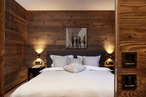 A bedroom with a wooden wall panel, a bed with white bedding, two bedside tables, and wall-mounted reading lights. - HAHNENKAMM SUITE DELUXE Wellnes & Ski-In/Ski-Out (Kitzbühel)