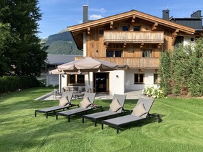 En stuga i trä med en balkong, en utomhusplats med sittmöbler och utsikt över bergen.