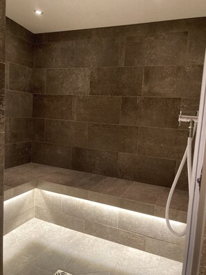 A modern shower area with dark tiles and a built-in bench. - HAHNENKAMM SUITE DELUXE Wellnes & Ski-In/Ski-Out (Kitzbühel)