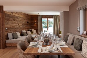 A dining area with a wooden table set for a meal, a sofa with cushions, and a view of the outdoors through a window. - HAHNENKAMM SUITE DELUXE Wellnes & Ski-In/Ski-Out (Kitzbühel)