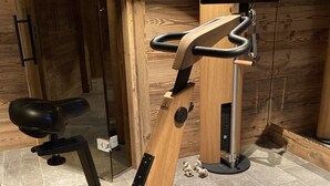 Ein stationäres Fahrrad mit Holzrahmen, schwarzem Sattel und einem digitalen Bildschirm, der an einer Wand angebracht ist.