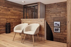 Ein modernes Zimmer mit Holzwänden, einer Holzauslage, zwei weißen Stühlen, einem schwarzen Laternen und zwei gerahmten Bildern an der Wand.