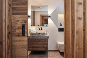 A modern bathroom with a wooden vanity, a sink, a mirror, and a toilet. - HAHNENKAMM SUITE DELUXE Wellnes & Ski-In/Ski-Out (Kitzbühel)