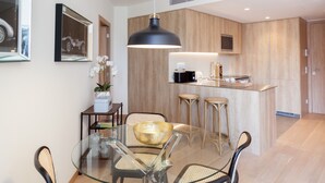 A modern kitchen with wooden cabinets, a glass dining table with four chairs, and a pendant light. - FLH Marquês Comfy Apartment (Lisbon)
