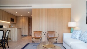 A modern hotel room with a wooden floor, a sofa, two leather chairs, a coffee table, a TV, and a kitchenette. - FLH Marquês Comfy Apartment (Lisbon)