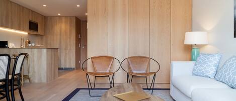 Una habitación de hotel moderna con piso de madera, un sofá, dos sillones de cuero, una mesa de centro, un televisor y una kitchenette.