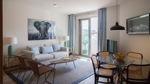 A modern living room with a sofa, coffee table, dining table, and chairs. There is a painting of an elephant on the wall, a lamp, and a window with curtains. - FLH Marquês Comfy Apartment (Lisbon)