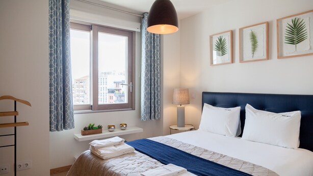 A neatly made bed with a blue blanket, a bedside lamp, and framed plant art on the wall. - FLH Marquês Comfy Apartment (Lisbon)