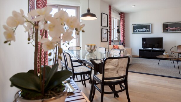 Una sala de estar moderna con una mesa de comedor de vidrio, sillas negras, un sofá y un televisor.