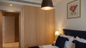 Una habitación de hotel con cama, almohadas, lámpara de noche, un cuadro en la pared y un armario.