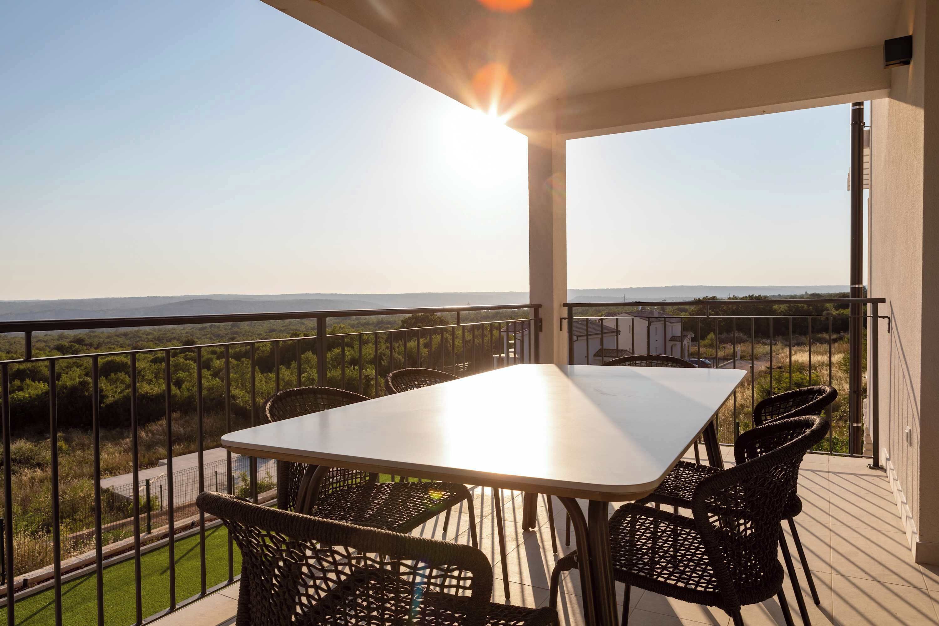A balcony with a table and chairs, a view of the landscape, and a clear sky.