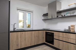 A modern kitchen with wooden cabinets, a black countertop, and a built-in dishwasher. - Villa Elysium (Sveti Lovrec Labinski)