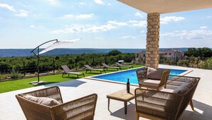 A poolside area with wicker furniture, a stone pillar, and a view of the sea. - Villa Elysium (Sveti Lovrec Labinski)