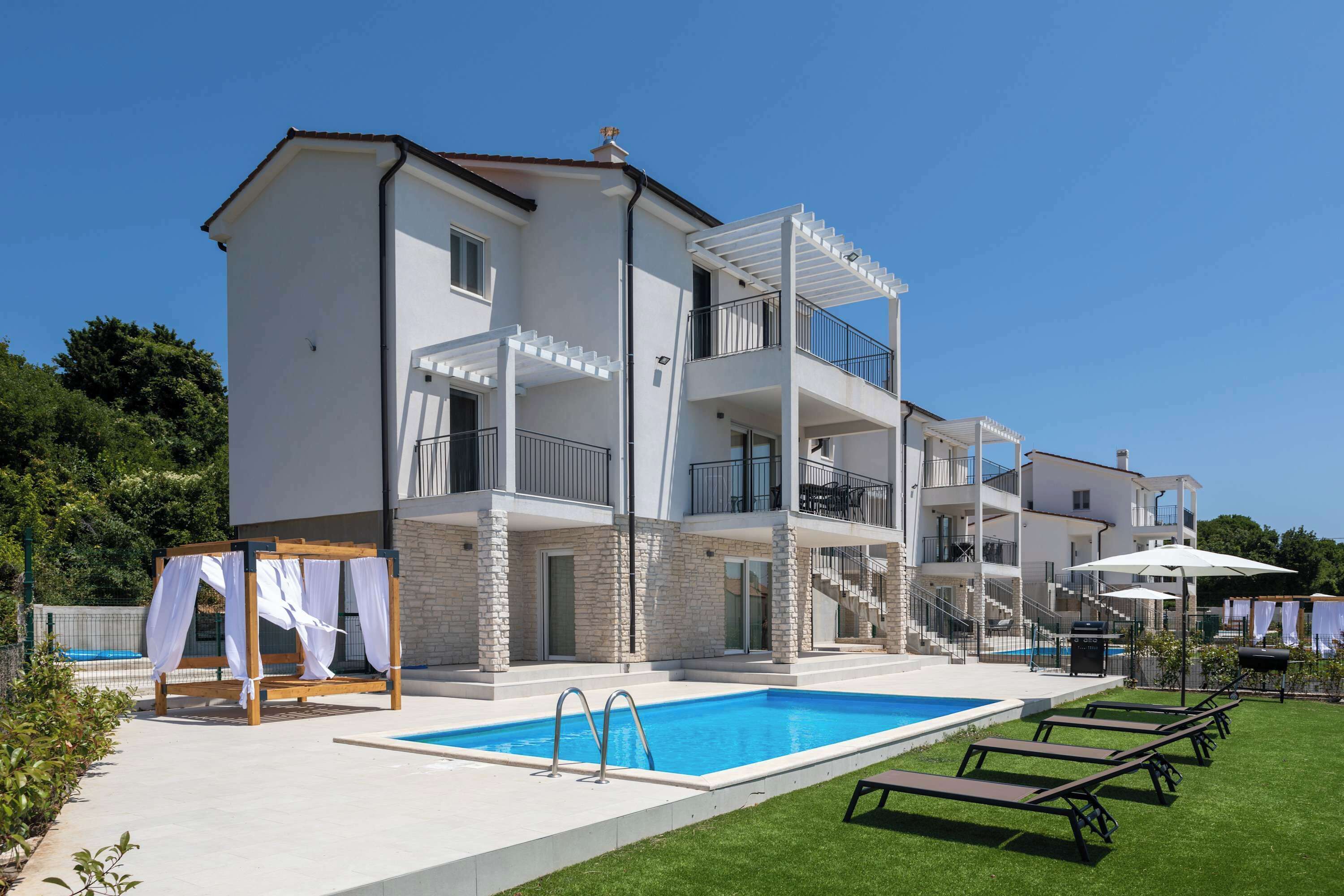 A multi-story building with a swimming pool, outdoor seating, and a covered patio area.