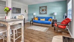 A living room with a blue sofa, a red chair, a wooden coffee table, and a dining table with chairs.