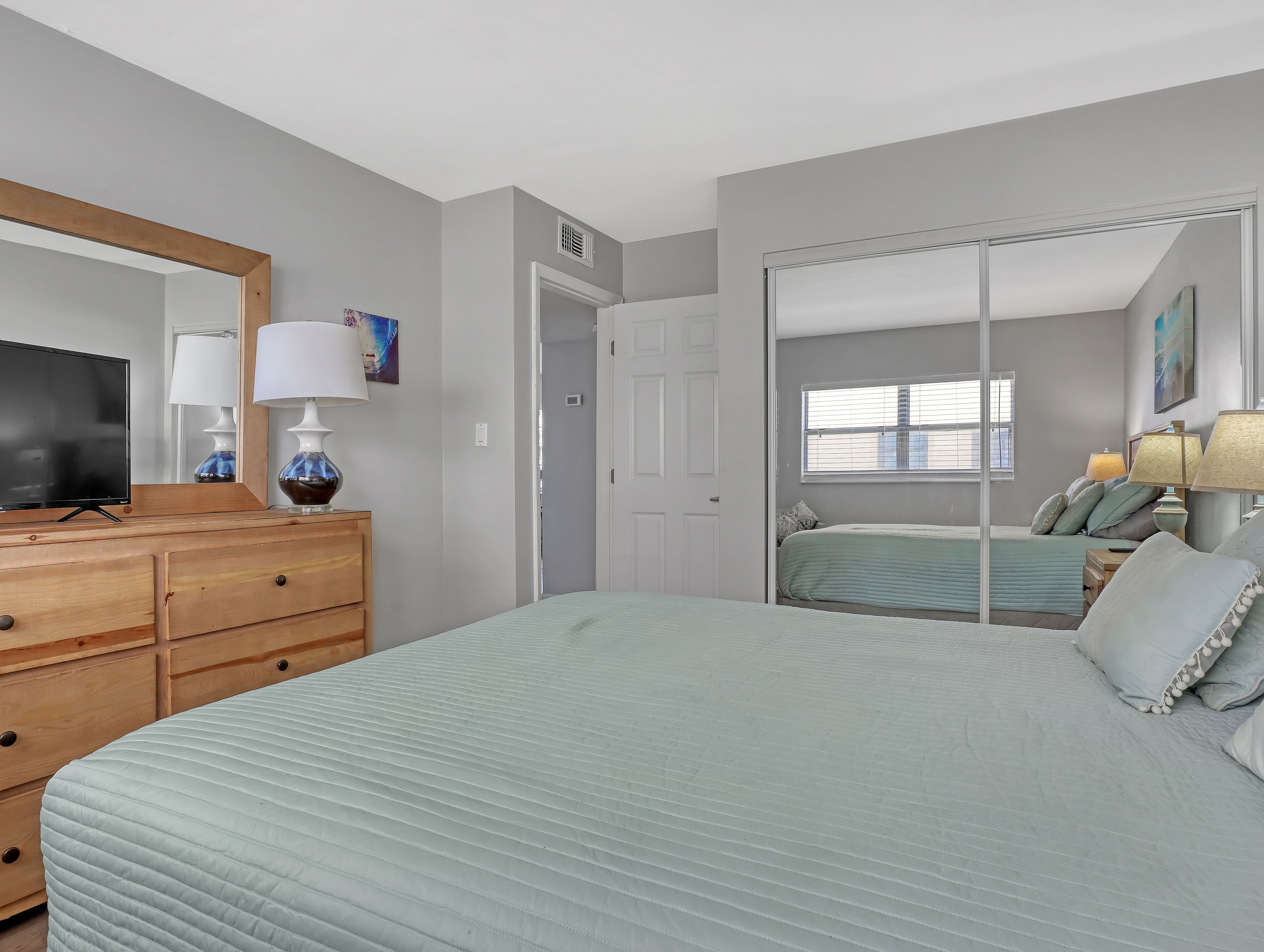 Een slaapkamer met een bed, een dressoir, een televisie en een spiegel.