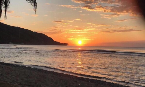 A beach with a sunset, calm water, and a distant landmass.