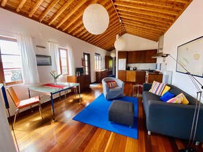 A spacious living area with a wooden ceiling, a dining table with chairs, a sofa with colorful cushions, and a kitchen in the background. - Quinta Perpetua, Casa Pico (Luz)
