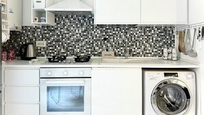 A compact kitchen with a microwave, oven, and washing machine, featuring a tiled backsplash and white cabinetry. - Central Rome Apartment near Termini | Walk to Major Attractions | Roman Haven (Roma)