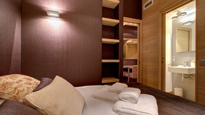 Une chambre d’hôtel avec un grand lit, une armoire en bois, une salle de bain avec un lavabo et un miroir, et une petite table avec une chaise.