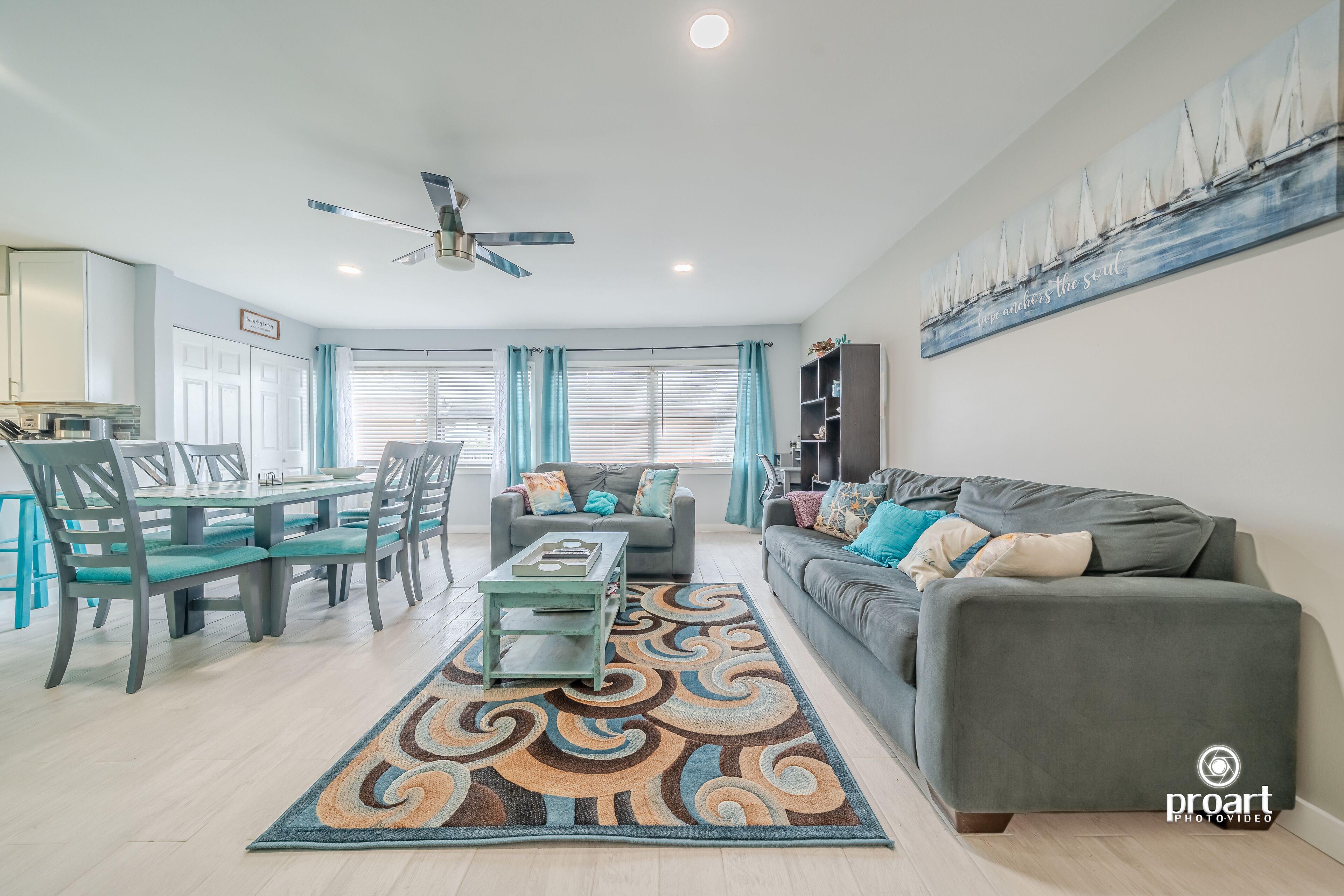 A modern living room with a grey sofa, teal chairs, a coffee table, and a patterned rug.