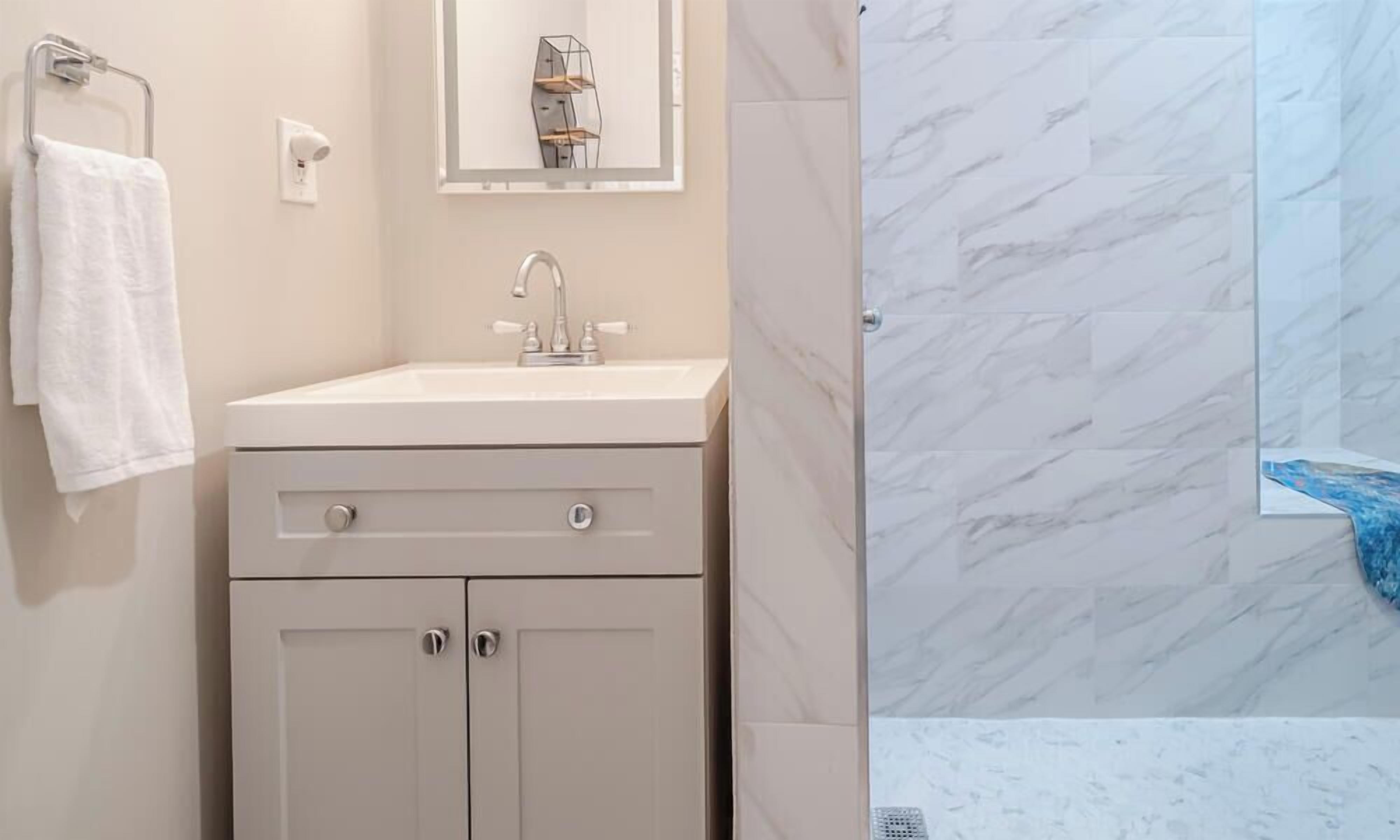 A bathroom with a white vanity, a mirror, and a shower with marble walls.
