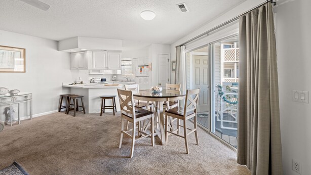 A spacious kitchen with white cabinets, a dining table with chairs, and a large sliding glass door leading to a balcony. - Shorehaven II 8B-2BR/2BA condo in Cherry Grove (North Myrtle Beach)