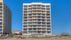 A multi-story hotel with balconies on each floor, a flat roof, and a clear blue sky in the background.