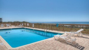 A swimming pool with clear blue water, surrounded by a wooden deck and white lounge chairs.