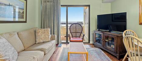 A living room with a sofa, a television, a wicker chair, and a view of the outdoors through a sliding door.