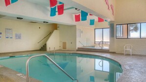 An indoor swimming pool with a clear view of the pool area, a staircase leading to a second level, and a window providing a view of the outside. - Sea Pointe 308 -Oceanfront 1BR- Indoor Pool & Hot Tub (North Myrtle Beach)