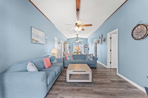 A living room with a sectional sofa, a coffee table, a ceiling fan, and a wall clock.