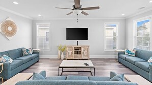 A modern living room with two sofas, a coffee table, a TV, and a ceiling fan. - Shore Am Happy - 5 Bedroom Luxury Home - Salt Water Pool (North Myrtle Beach)