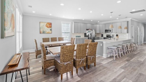 A spacious kitchen with modern appliances, a dining area with wicker chairs, and a large island with bar stools. - Shore Am Happy - 5 Bedroom Luxury Home - Salt Water Pool (North Myrtle Beach)