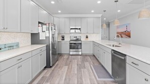 A modern kitchen with grey cabinets, stainless steel appliances, and a wooden floor. - Shore Am Happy - 5 Bedroom Luxury Home - Salt Water Pool (North Myrtle Beach)