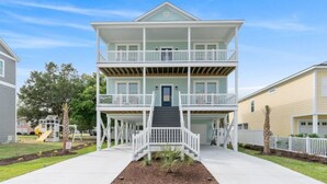A two-story residential building with a balcony on each floor, a front porch, and a driveway leading to the entrance. - Shore Am Happy - 5 Bedroom Luxury Home - Salt Water Pool (North Myrtle Beach)