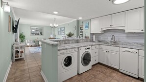A modern kitchen with white cabinetry, a built-in washer and dryer, and a marble countertop.